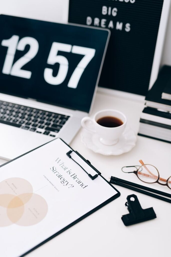 Stylish workspace featuring a laptop, clipboard with brand strategy, and coffee cup for a creative work environment.